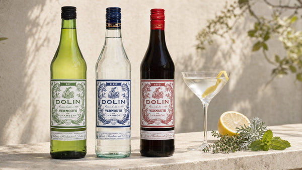 Dolin Dry, Dolin Blanc and Dolin Rouge vermouths on a stone bench beside a Dry Martini, lemon and alpine herbs
