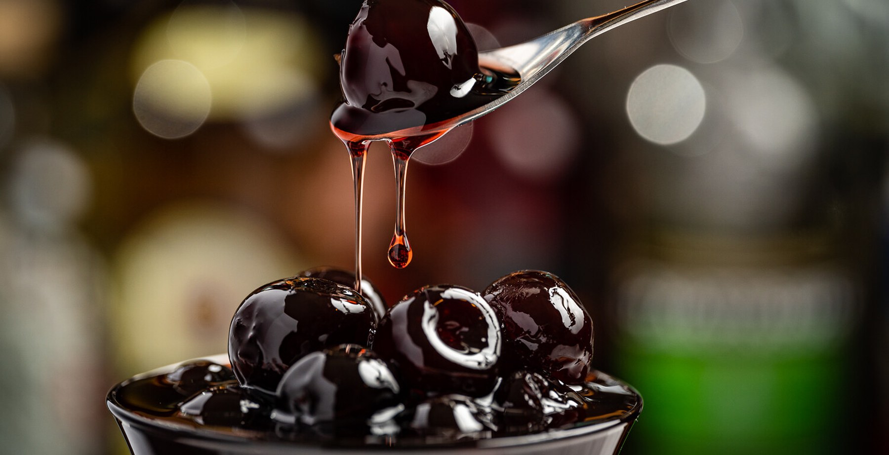 Cocktail cherries in syrup being lifted from a bowl with a bar spoon