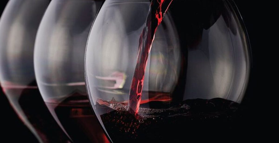 Red wine being poured into a row of glasses against a dark background